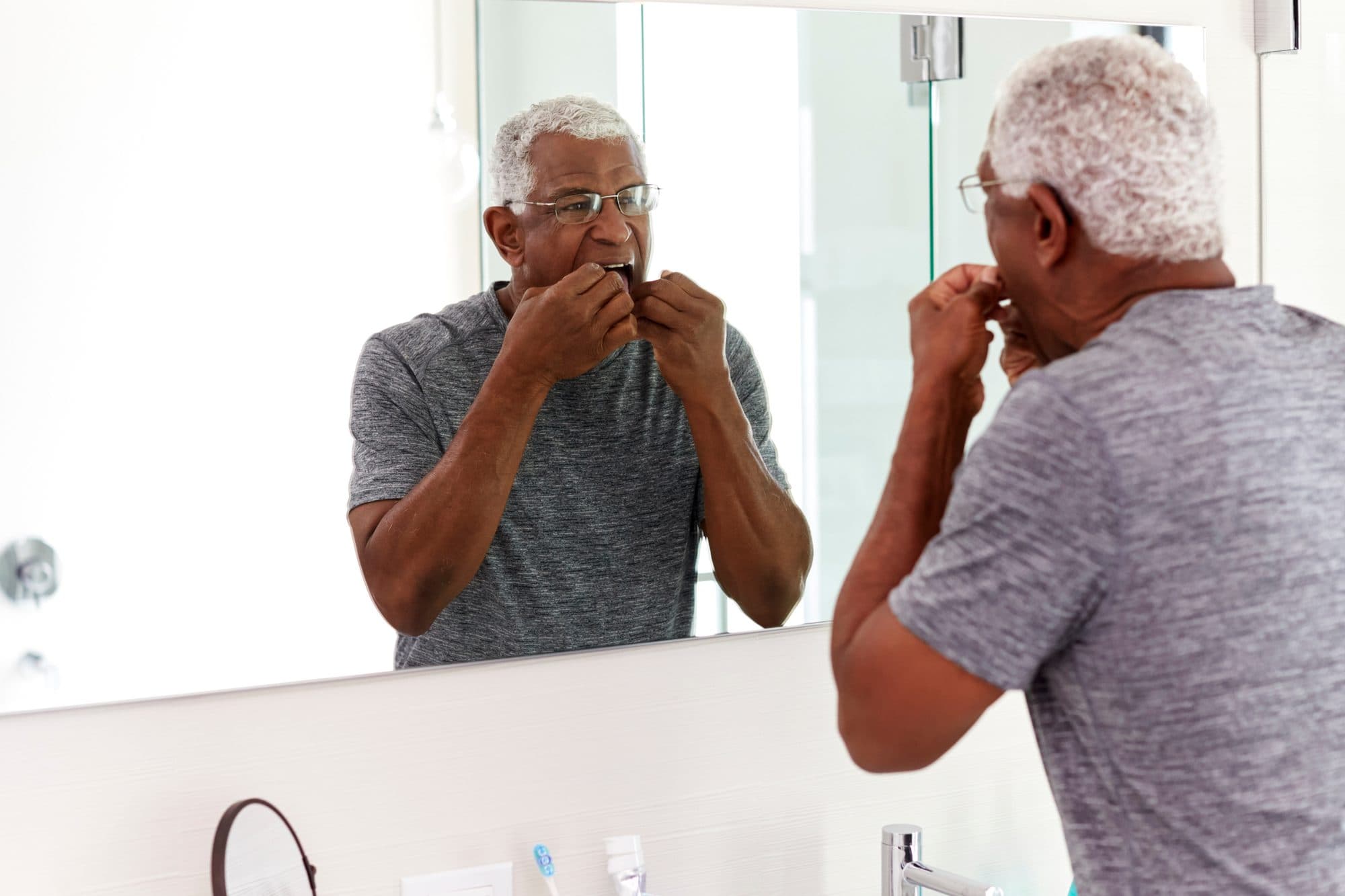 An older man getting ready in front of the bathroom mirror.