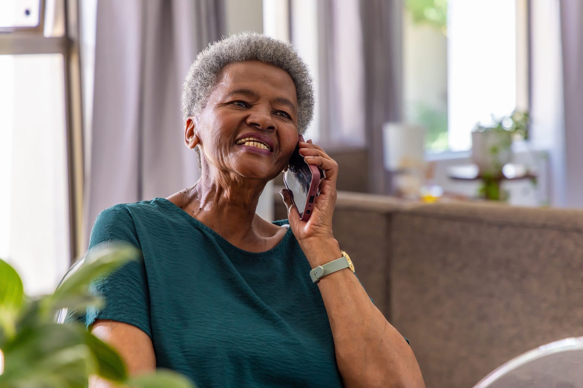 An older woman at home, laughing while talking on her phone.